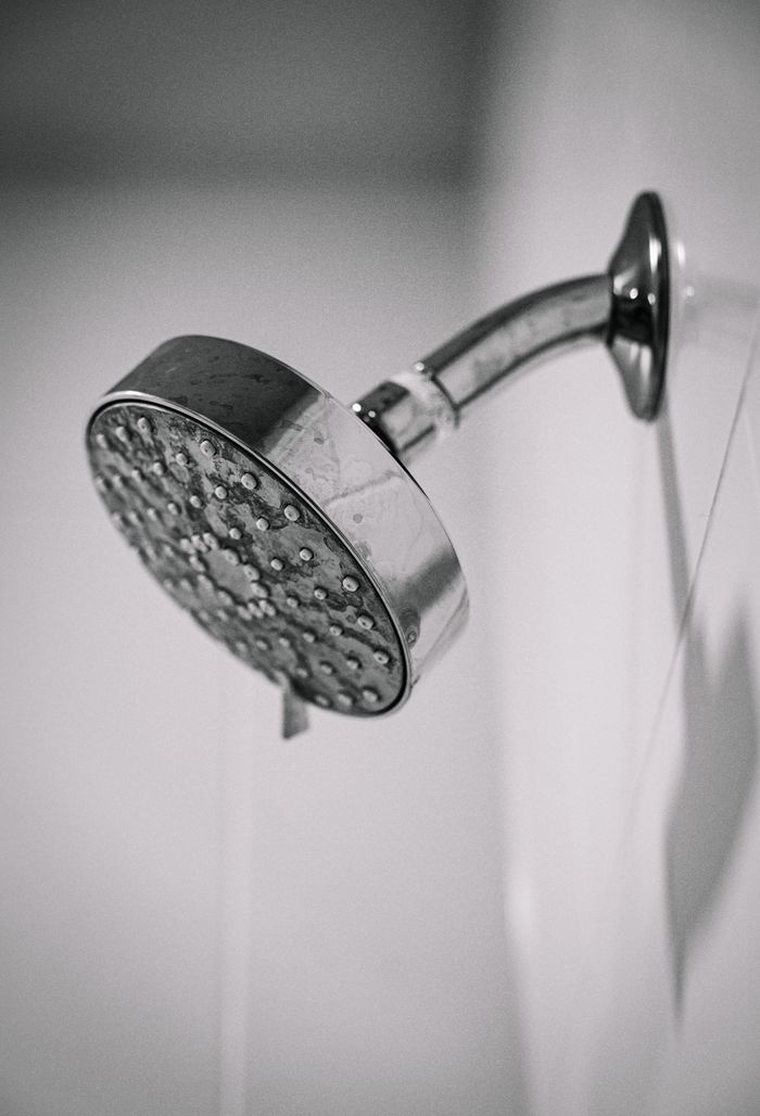 Black and white photo of a sleek, metal showerhead mounted on a bathroom wall.